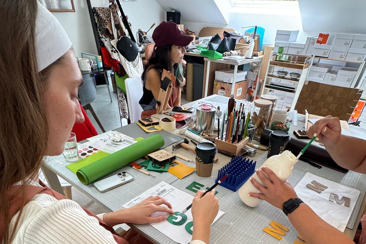 Two people working at a table with various items including a phone, cup, and tools.
